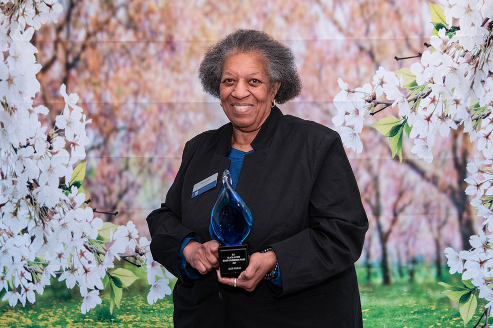 Alice Stanley poses for a photo with an award in front of a floral background.