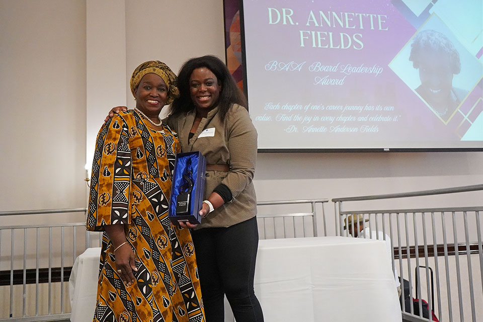 Annette Fields poses for a photo with an award on a stage.