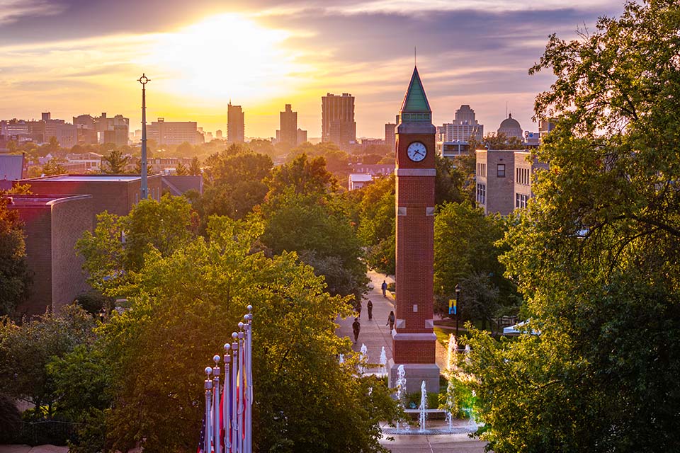 A clock tower on campus with the sun setting behind it.