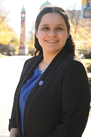 A headshot photo of Andrea Sedano with a clocktower and trees in the background.