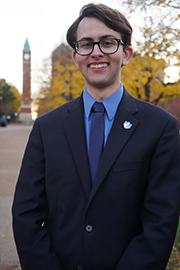 Headshot photo of Chris Brault with a clocktower and trees in the background.