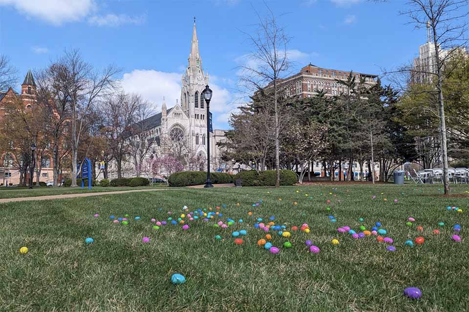 Colorful easter eggs spread out on a green lawn with College Church and Dubourg Hall in the background on a sunny day