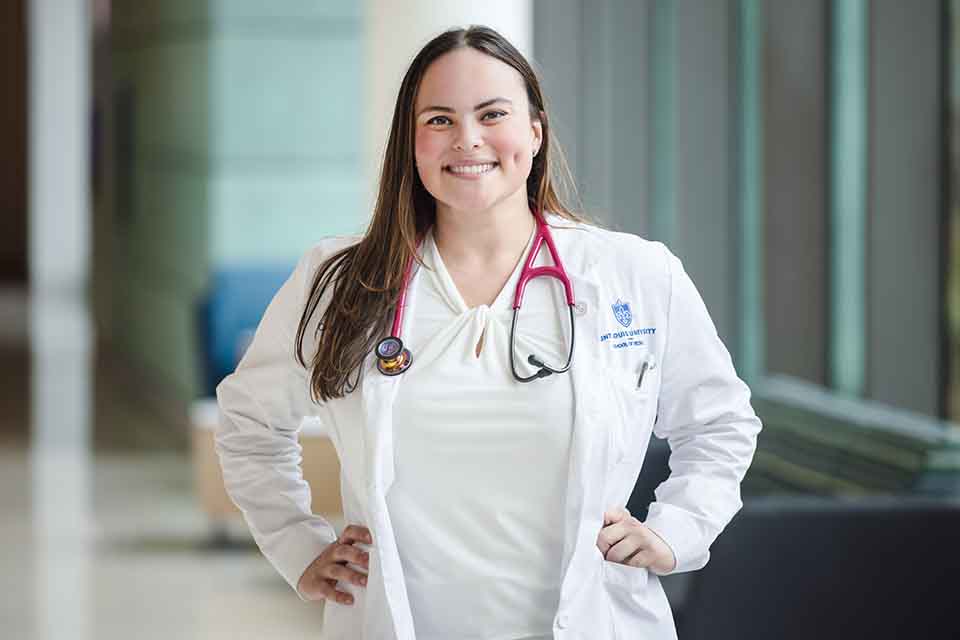 Caroline Wright poses for a photo in the hallway of a medical building wearing a doctor's white coat.