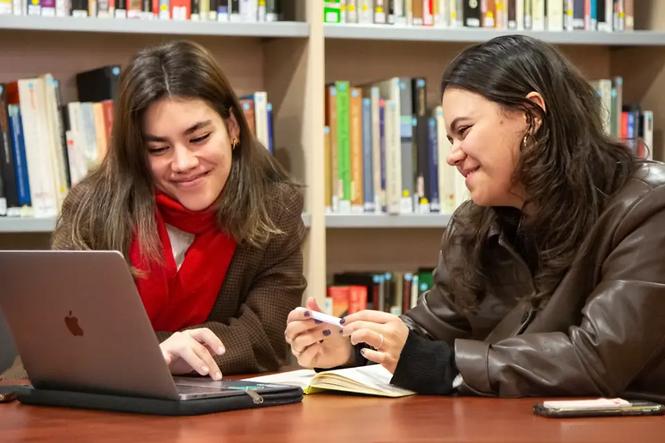 Two students sitting at a table with a laptop in the library.