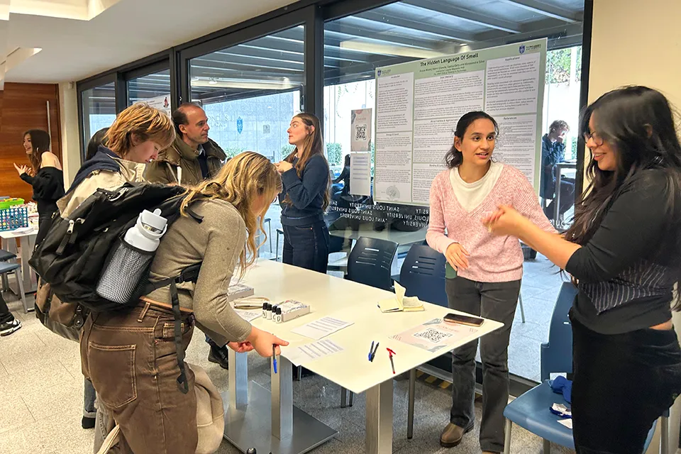 Two people look down while filling out a form while looking at essential oil bottles. Two girls talk to event participants behind a table and a poster in the background shows research details. 