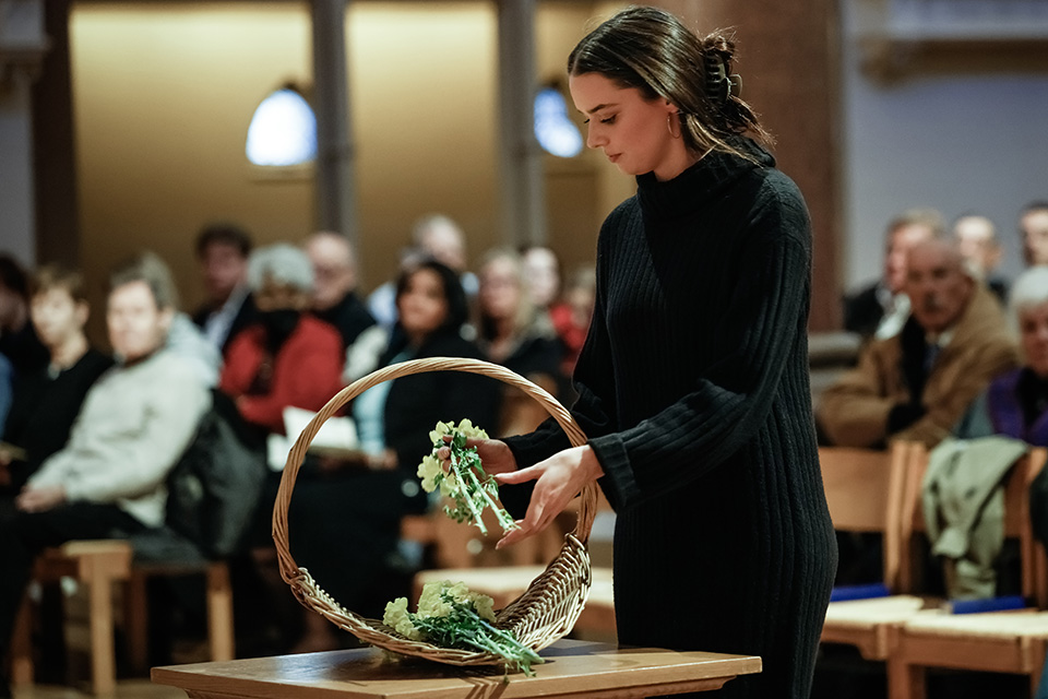 A young woman places flowers in a basket during a prayer service.