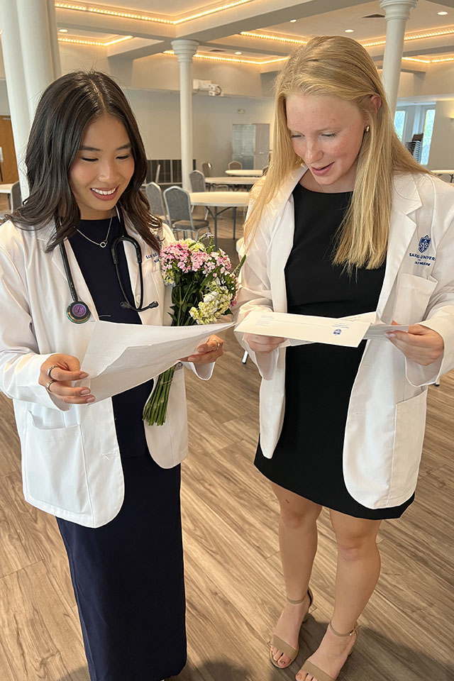 M1 students read notes of encouragement from SLU alumni. Two female medical students excitedly read notes of encouragement from alumni.