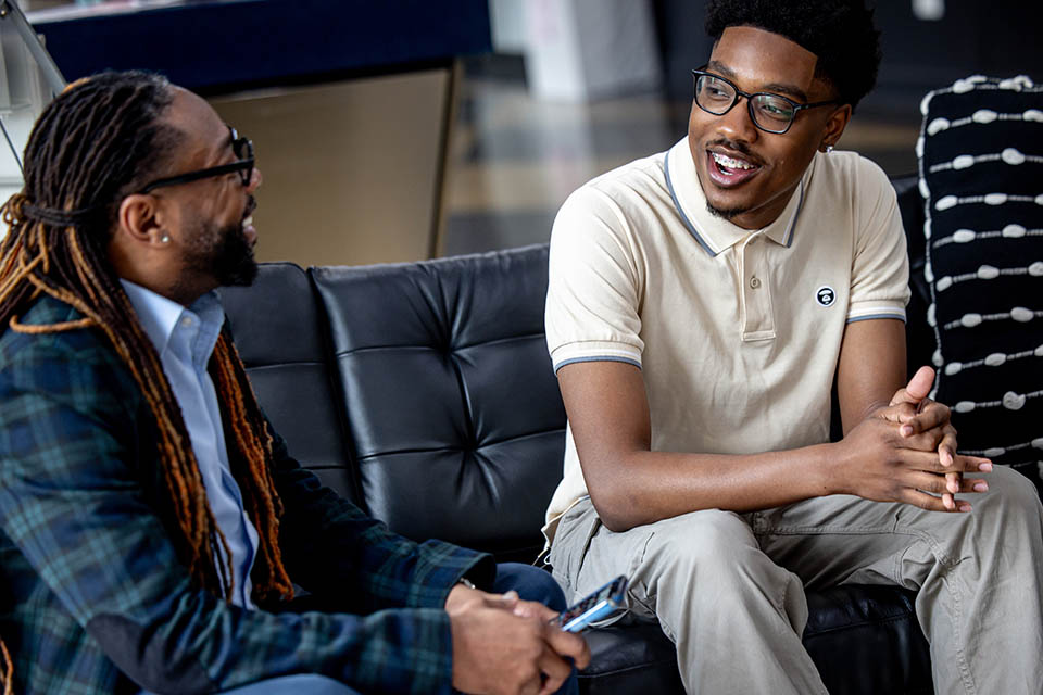 African American Male Scholars mentor Dr. Richard Marks, left, meets with student Russell Hooker Jr. on April 26, 2024. They are sitting on a black couch inside a room. 