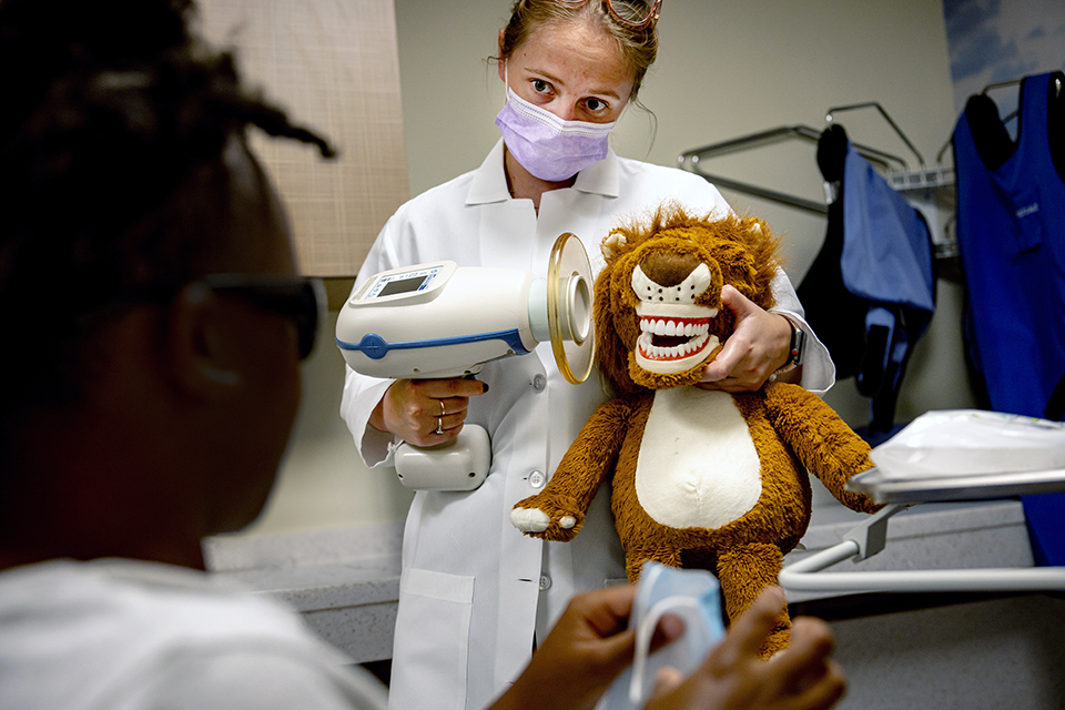 Resident Katelyn Glaenzer holds a stuffed lion. She models a dental exam for a pediatric patient.