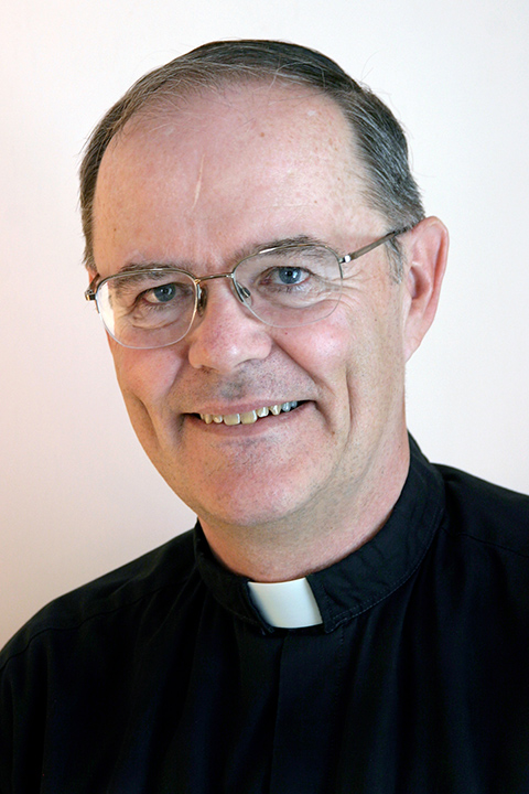An older white man wearing glasses and a Catholic priest's Roman collar